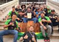 Equipe brasileira campeã mundial de churrasco reunida na escadaria exibindo medalhas, troféus e certificado da conquista.