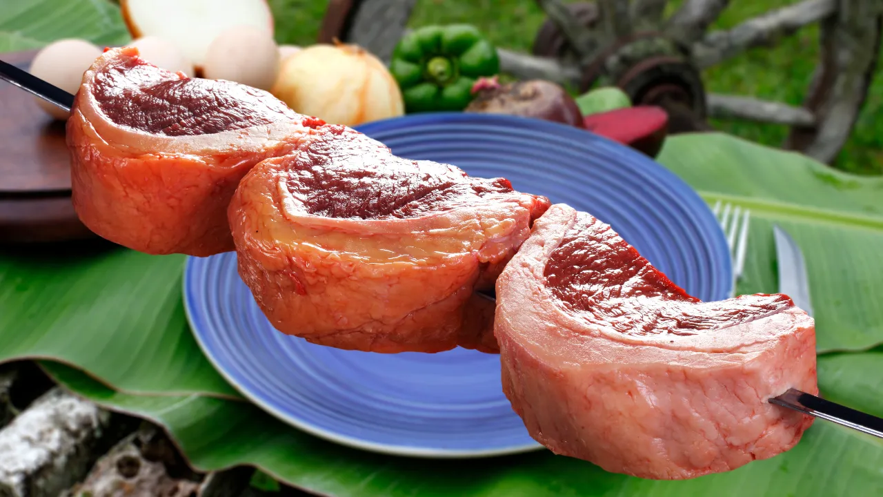 Fatias de picanha fresca montadas no espeto, destacando a coloração intensa da carne e a camada de gordura típica do churrasco brasileiro.